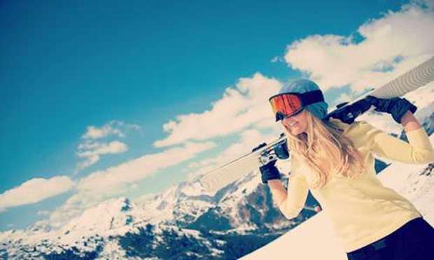 Blue sky with clouds over a snow-capped mountain with a woman carrying a ski on her shoulders. Explore Andorra Hen Party ideas below: